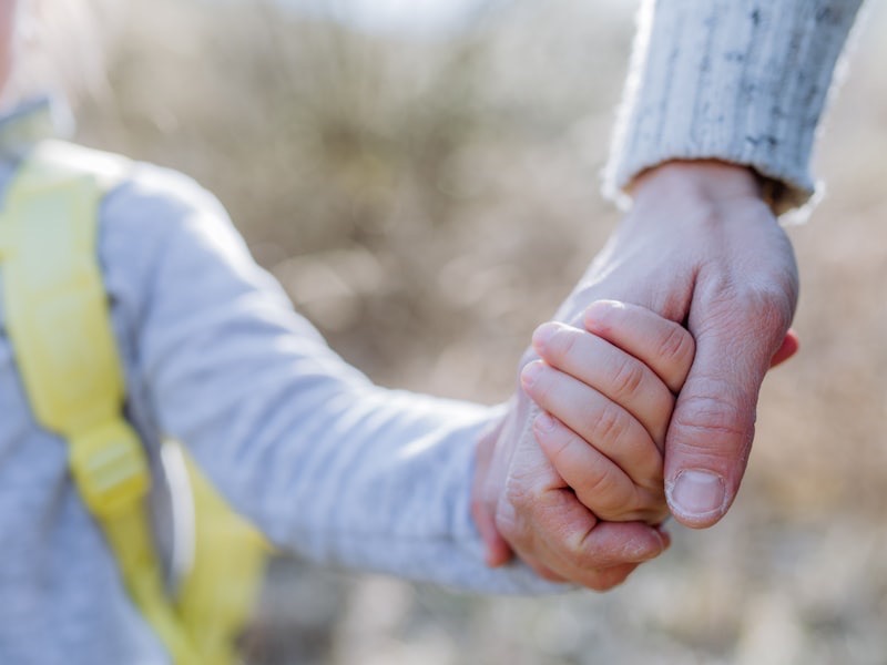 An adult and a child holding hands while walking together outdoors