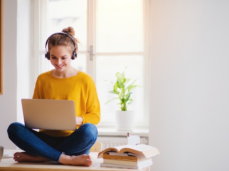 A teenager in a green hoodie focused on a laptop at a desk