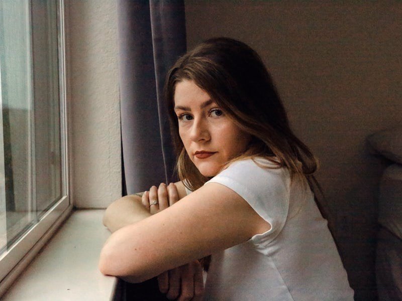 A thoughtful teenager sitting near a bright window in soft, warm light